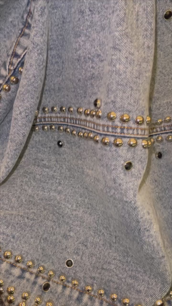 Collared, light to medium blue, stonewashed, denim, bolero style jacket with silver ball studs and black and silver jeweled studs sewn into the jacket and securely affixed. This jacket is a cropped type of style that stops mid back. No button closure, zipper or snaps. Worn in the same fashion as a shrug. Perfect for the times when you want to stay warm but still keep it cute and sexy to show off your torso and bottom. Quality craftsmanship, design and fabric used throughout. 