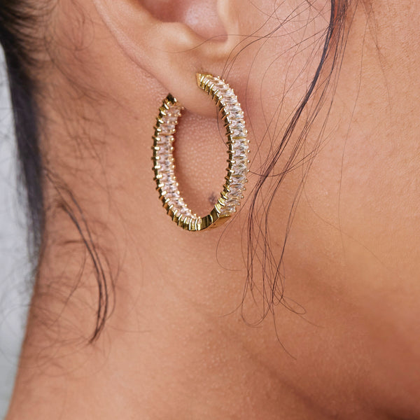 There's nothing like a good baguette, diamond hoop and the Baguette Me Earrings are a must add to any collection!   1" circumference, 18k gold plating with baguette A+++ CZ stones surrounding the entire earring.  Expect to get up to 1 year worth of tarnish proof, water resistant wear from our jewelry with proper care. Hypoallergenic.