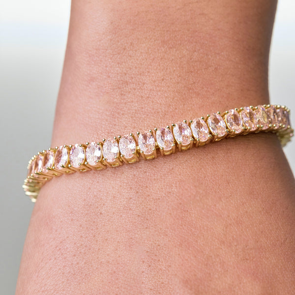Who doesn't love pink? This tennis bracelet is the cutest shade of baby pink. We love the unique oval shaped stones, heavyweight and quality detailing of this piece. The Pink Sorbet Tennis Bracelet does not disappoint!  7" in length with clear pink, brilliant, oval shaped, 5mm A+++ CZ crystal stones. Push button box clasp closure.  18k gold plating  Expect to get up to 1 year worth of tarnish proof, water resistant wear from our jewelry with proper care. Hypoallergenic.