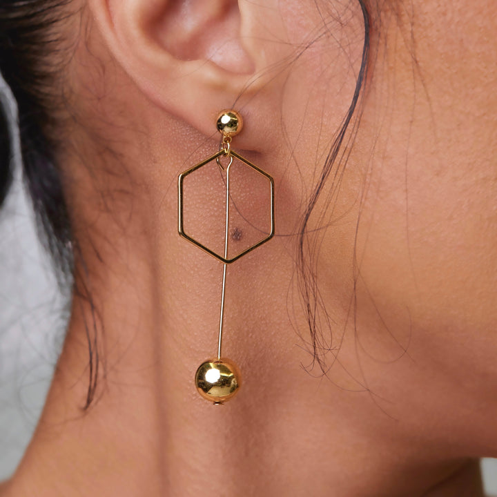 Who can really resist these unique and head turning stunners? The Mix It Up Earrings make a statement all on their own!   Handmade, 14k gold plated, drop earrings in a mis-match design. *Be aware that all of our handmade pieces are unique and individual with slight variations to each piece.  One earring drops into a circular ball pattern with the other earring sporting a dangling hexagon near the post that drops down to a ball.   Tarnish resistant and water resistant with proper care. Hypoallergenic.