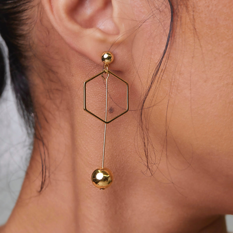 Who can really resist these unique and head turning stunners? The Mix It Up Earrings make a statement all on their own!   Handmade, 14k gold plated, drop earrings in a mis-match design. *Be aware that all of our handmade pieces are unique and individual with slight variations to each piece.  One earring drops into a circular ball pattern with the other earring sporting a dangling hexagon near the post that drops down to a ball.   Tarnish resistant and water resistant with proper care. Hypoallergenic.